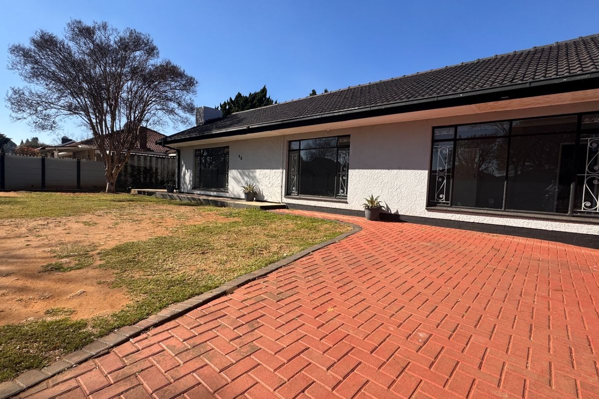 Rear view of the house featuring a tiled roof, large windows with security bars, and a brick-paved patio area leading to the garden.