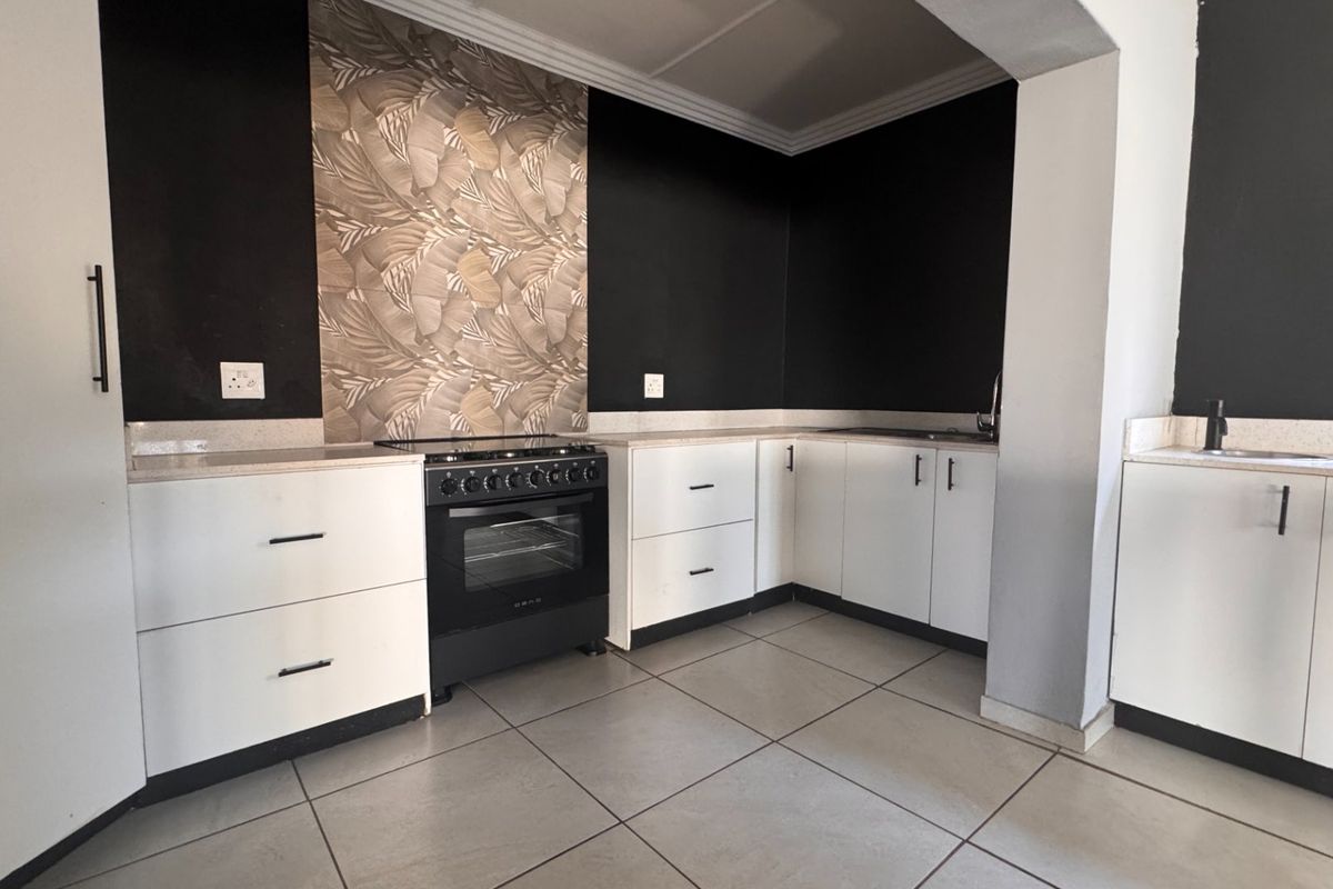 A modern kitchen featuring white cabinetry, stone countertops, a black freestanding oven, and decorative feature wall tiling.