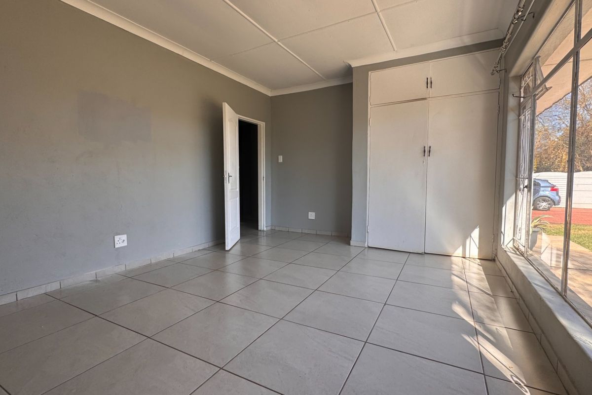 An empty bedroom featuring tiled flooring, built-in cupboards, and large windows providing natural light and garden views.