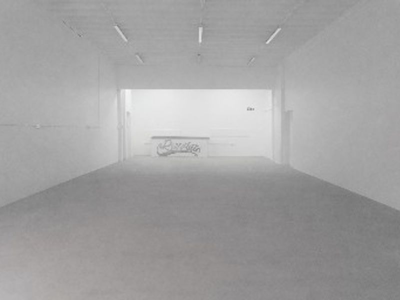 An expansive, empty industrial utility space featuring concrete flooring, fluorescent strip lighting, and a built-in service counter at the rear.