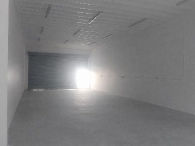 A spacious, empty industrial utility area featuring concrete flooring, a corrugated metal ceiling, and a secure roller shutter door.