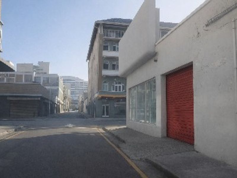 Street view of an industrial property featuring a prominent red roller shutter door and a large display window along the sidewalk.