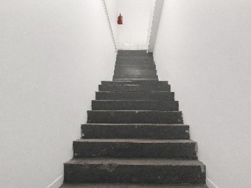 A functional industrial concrete staircase leading upwards, featuring a wall-mounted fire extinguisher.