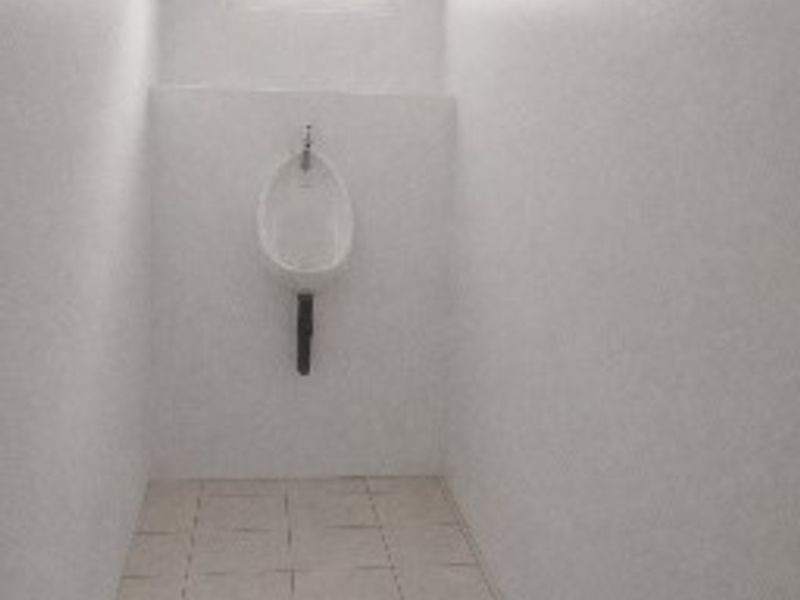 A simple, functional restroom facility featuring a wall-mounted urinal, tiled flooring, and a small window for natural light.