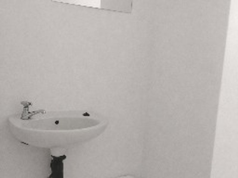 A functional bathroom space featuring a wall-mounted basin, chrome faucet, wall mirror, and a safety grab rail.