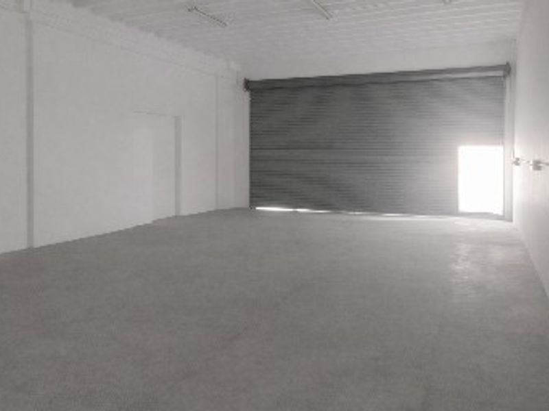Spacious industrial utility area featuring concrete flooring, white walls, and a large roller shutter door for easy access.