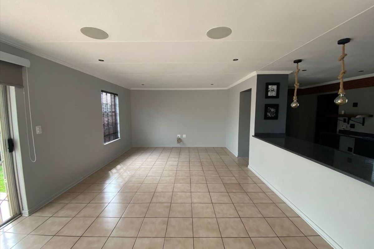 Spacious open-plan living area featuring neutral tiled flooring, recessed ceiling speakers, and a breakfast bar counter connecting to the kitchen space.