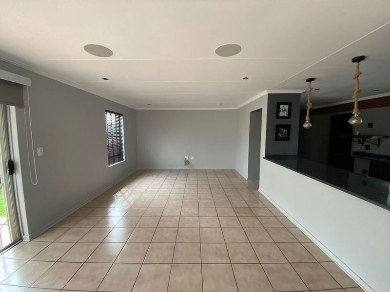 Spacious open-plan living area featuring neutral tiled flooring, recessed ceiling speakers, and a breakfast bar counter connecting to the kitchen space.