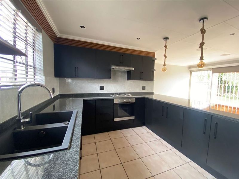 Modern kitchen featuring sleek dark cabinetry, granite countertops, built-in oven, gas hob, and a double basin sink with tiled flooring.