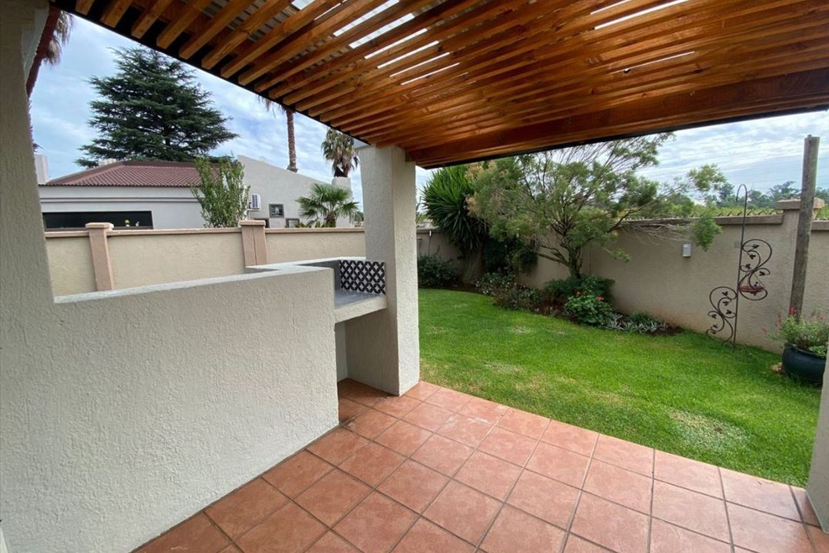Covered patio area featuring a wooden pergola, built-in braai, and tiled flooring, overlooking a private garden with a boundary wall.