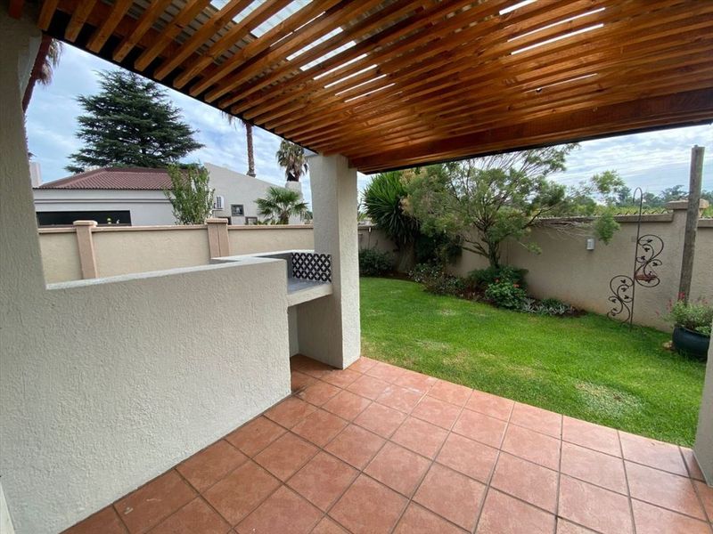 Covered patio area featuring a wooden pergola, built-in braai, and tiled flooring, overlooking a private garden with a boundary wall.