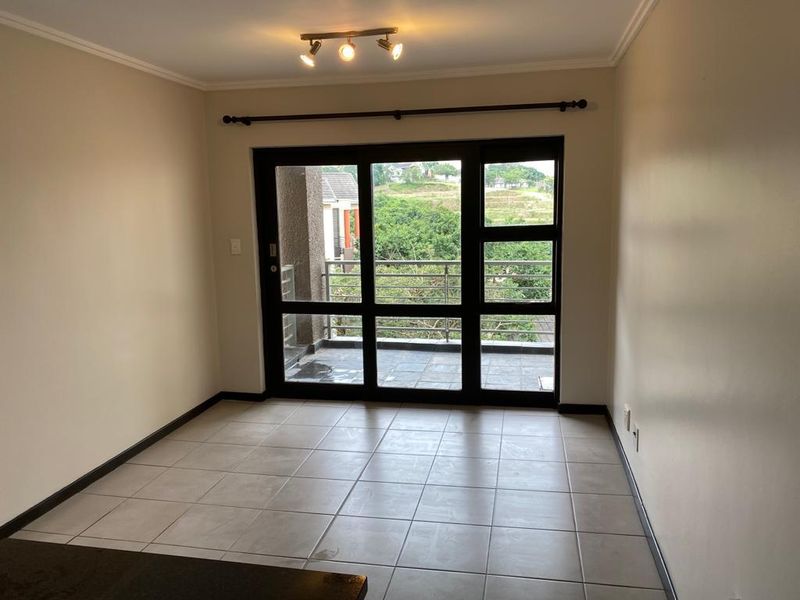 An empty living room featuring neutral tiled flooring and large glass sliding doors that provide access to an outdoor balcony area.