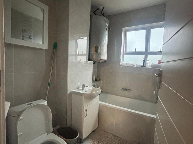 A functional bathroom featuring a bathtub, vanity basin, and toilet with tiled finishes and an exposed electric water heater.