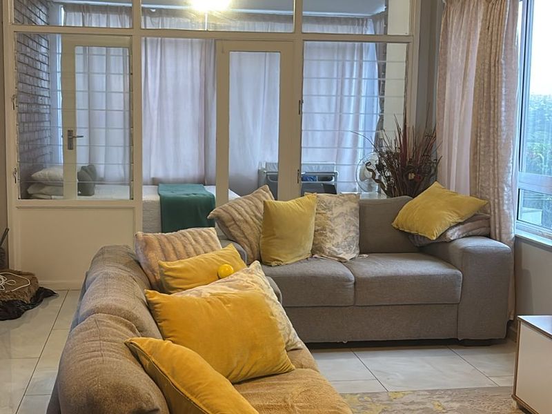 A comfortable living room featuring tiled flooring and a large glass partition wall that separates the space from an adjacent room.