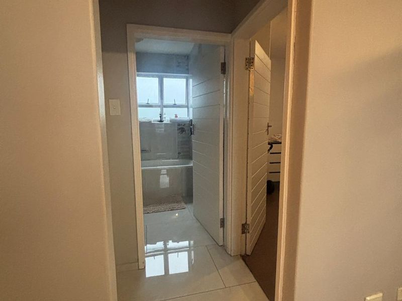 A view through a hallway leading to a bathroom, featuring tiled flooring and neutral wall finishes.