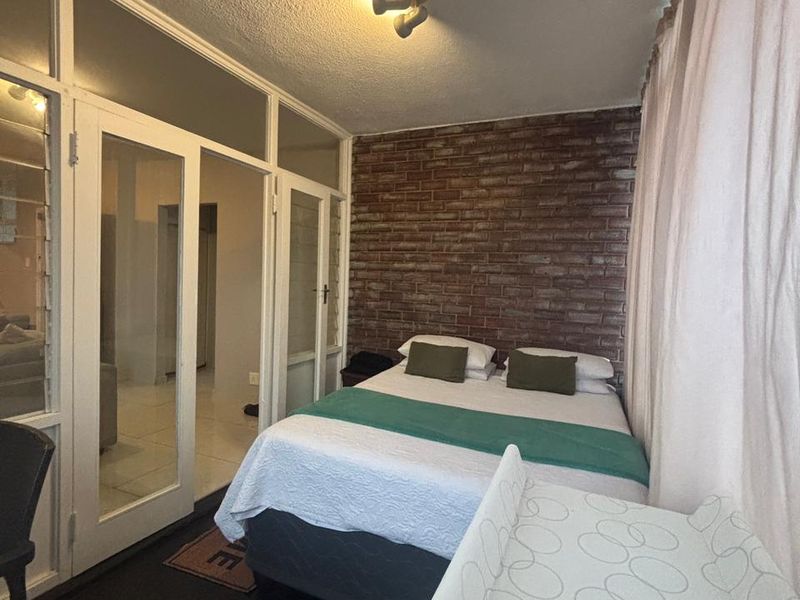 Bedroom featuring an exposed brick feature wall, glass panel doors, and louvered windows, offering a unique architectural aesthetic.