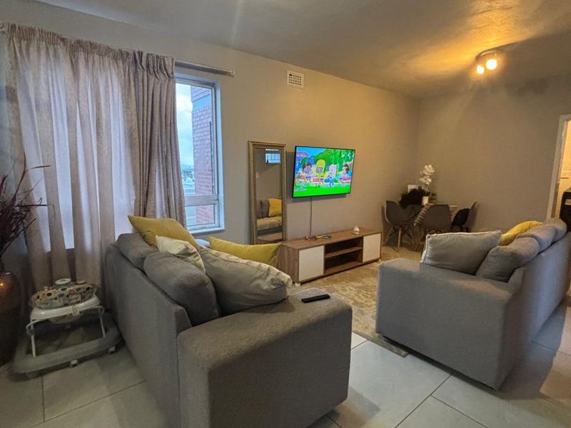 A comfortable living room featuring large format floor tiles, neutral wall tones, and ample natural light from a large window.