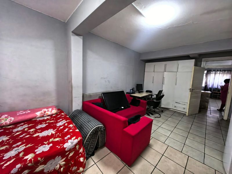 A multi-purpose living area featuring built-in white cabinetry, tiled flooring, and a structural support beam, offering potential for versatile use.