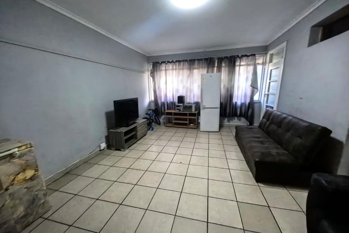 A spacious living area featuring neutral floor tiles, coved ceilings, and large windows allowing for natural light.