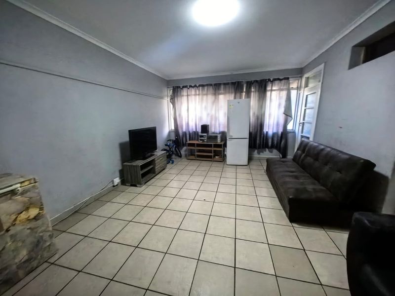 A spacious living area featuring neutral floor tiles, coved ceilings, and large windows allowing for natural light.
