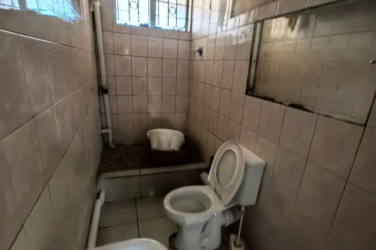 A compact bathroom featuring a toilet, sink, and tiled walls, requiring modernization and maintenance to improve its overall condition and functionality.
