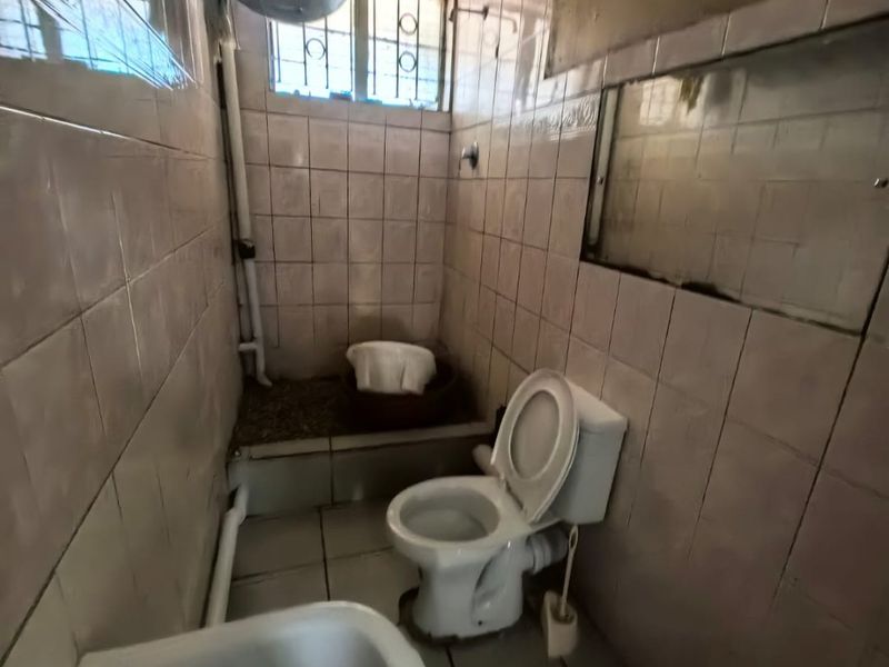 A compact bathroom featuring a toilet, sink, and tiled walls, requiring modernization and maintenance to improve its overall condition and functionality.