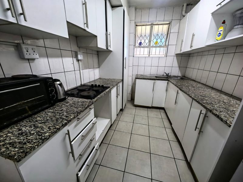 Functional kitchen featuring white cabinetry, granite-look countertops, tiled walls, and a built-in electric hob.