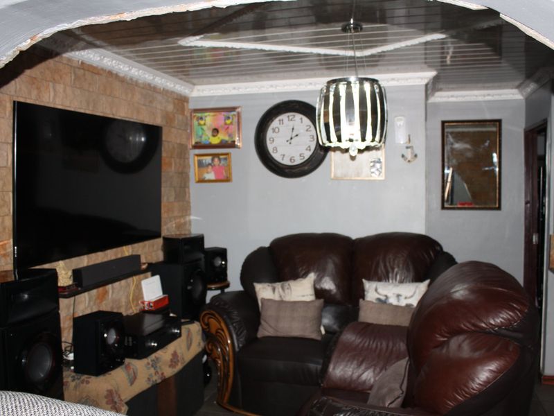 A living room featuring a stone-clad feature wall, a suspended ceiling with decorative molding, and an arched entryway.