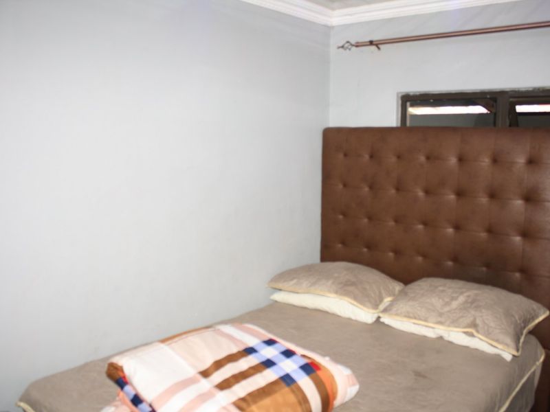 A bedroom featuring a tufted brown headboard and a window with a curtain rod.