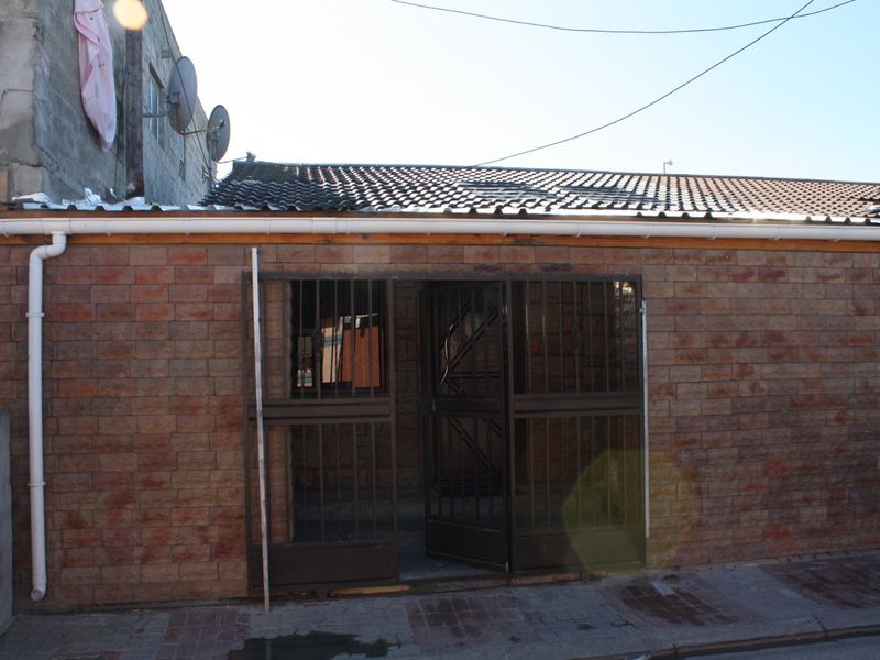 Exterior view of a brick-faced residential structure featuring a metal security gate entrance and tiled roof.