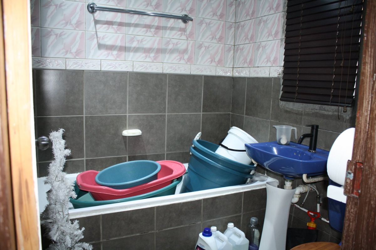 A compact bathroom featuring a bathtub, pedestal basin, and tiled walls. The space requires cosmetic updates to modernize the finishes.