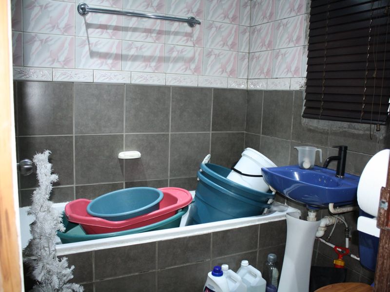 A compact bathroom featuring a bathtub, pedestal basin, and tiled walls. The space requires cosmetic updates to modernize the finishes.