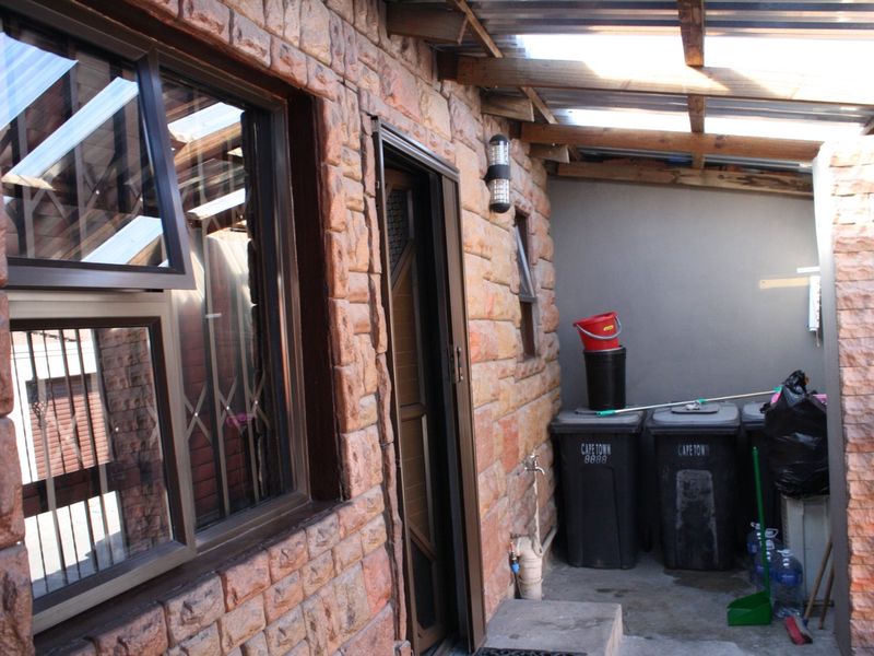 A covered outdoor utility area featuring stone-clad walls, a translucent roof structure, and a secure window with security bars.