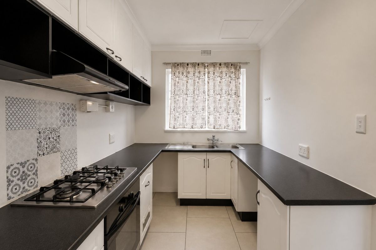 A clean and functional kitchen featuring white cabinetry, dark countertops, a gas hob, built-in oven, and decorative backsplash tiling.