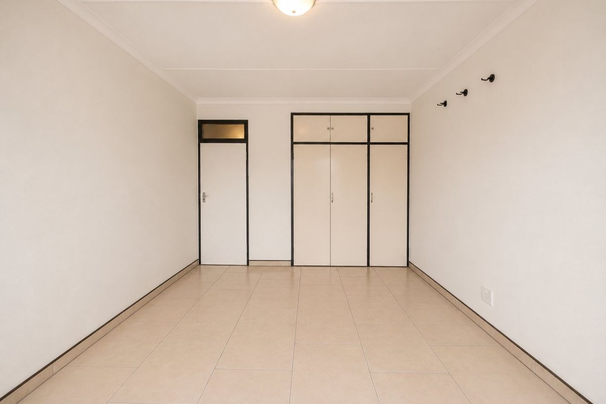 An empty bedroom featuring neutral tiled flooring, built-in cupboards, and a simple ceiling light fixture.