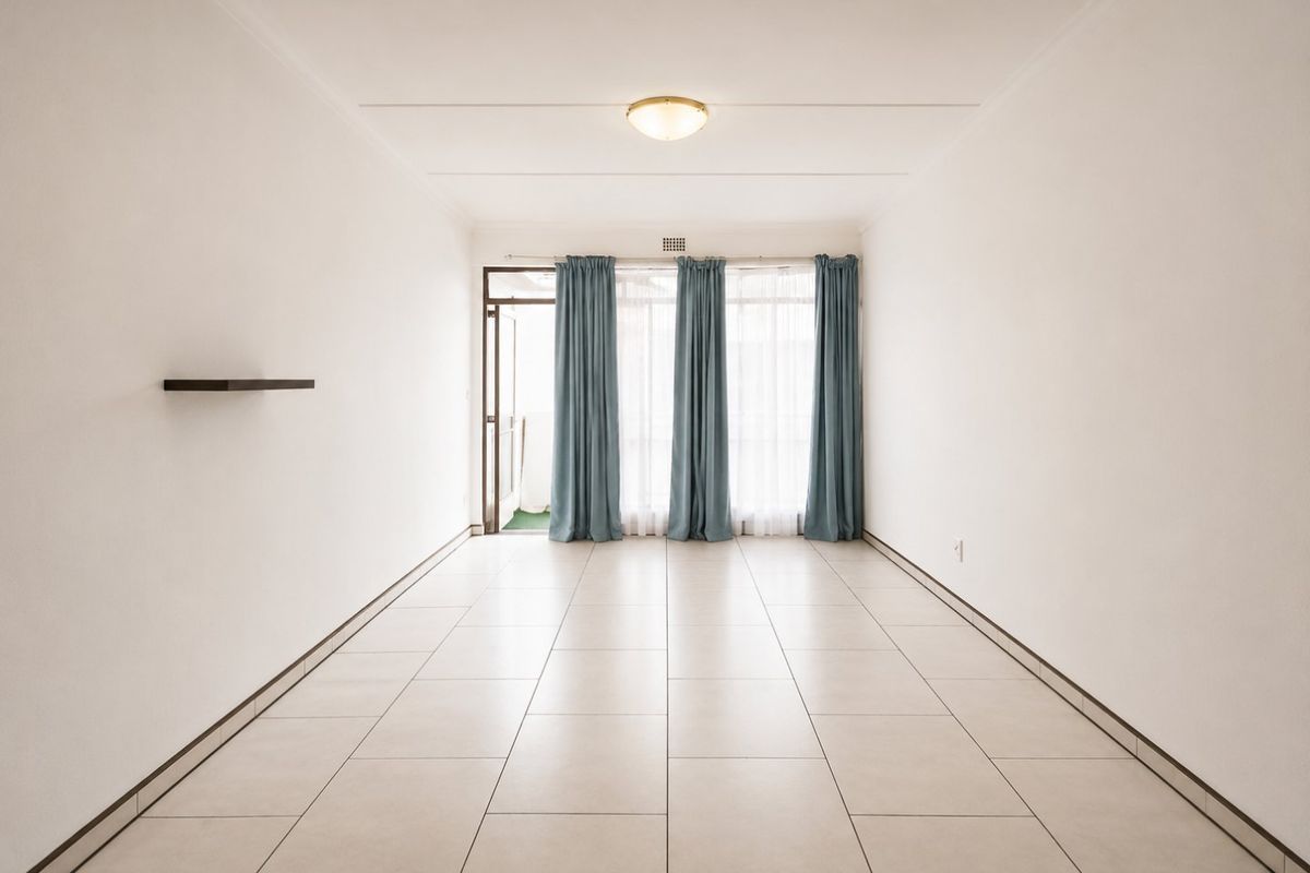 A bright, empty living room featuring neutral tiled flooring, a ceiling light fixture, and a sliding glass door leading to an outdoor area.