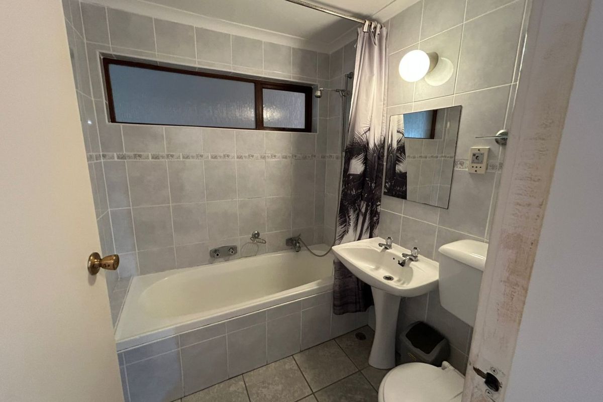 A functional bathroom featuring a bathtub with shower attachment, pedestal sink, toilet, and neutral wall and floor tiling.