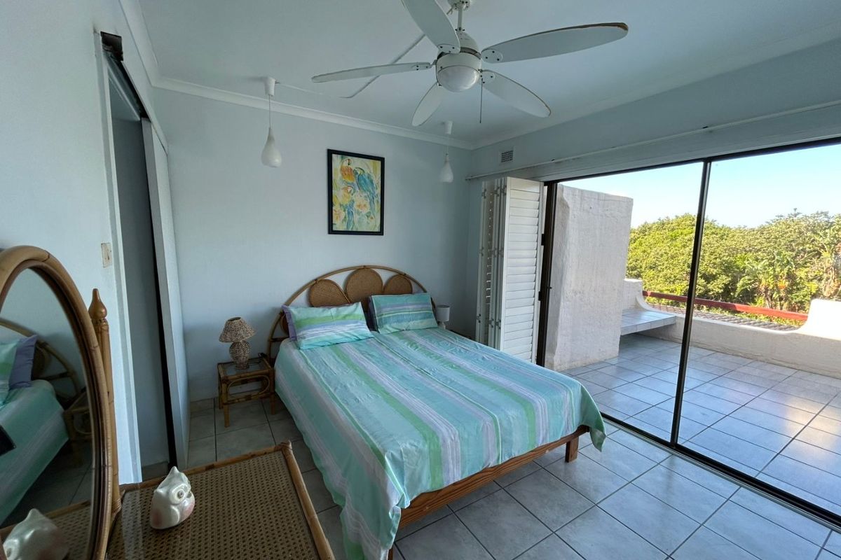 A bright bedroom featuring tiled flooring, a ceiling fan, and large sliding glass doors that open onto a private balcony.