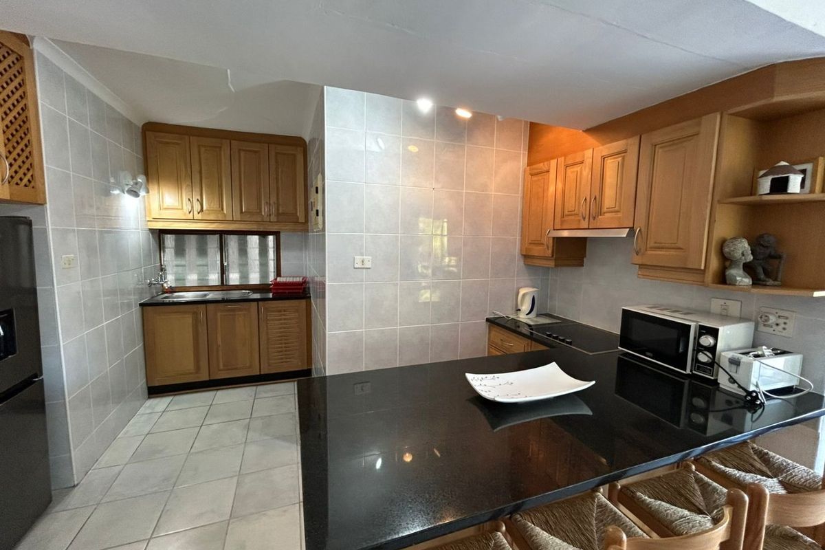 A functional kitchen featuring wooden cabinetry, black granite countertops, a breakfast bar, and tiled finishes throughout.
