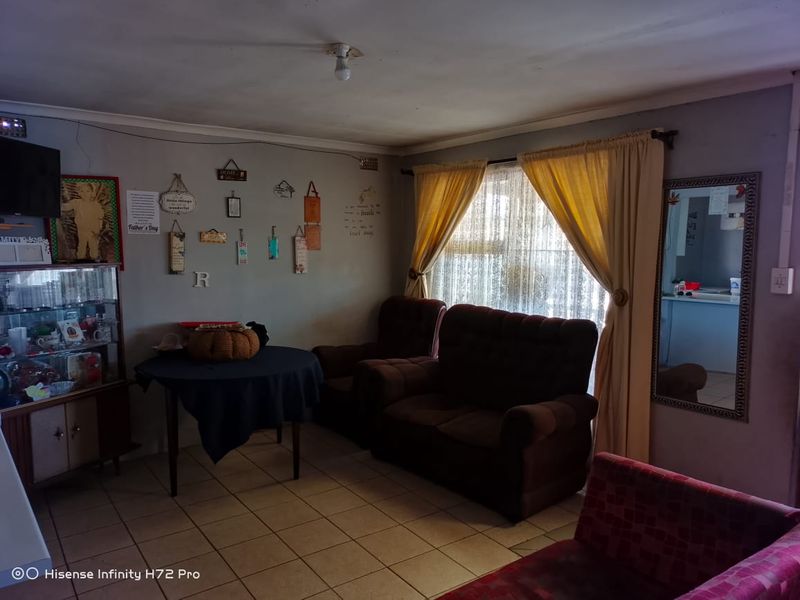A living room featuring tiled flooring and curtain rails, currently showing signs of wear including ceiling cracks and peeling paint.