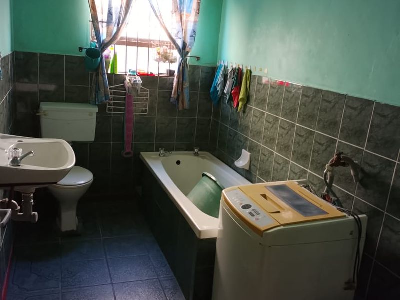 A dated bathroom featuring a bathtub, toilet, and pedestal basin with dark tiled walls and flooring, requiring cosmetic updates and maintenance.