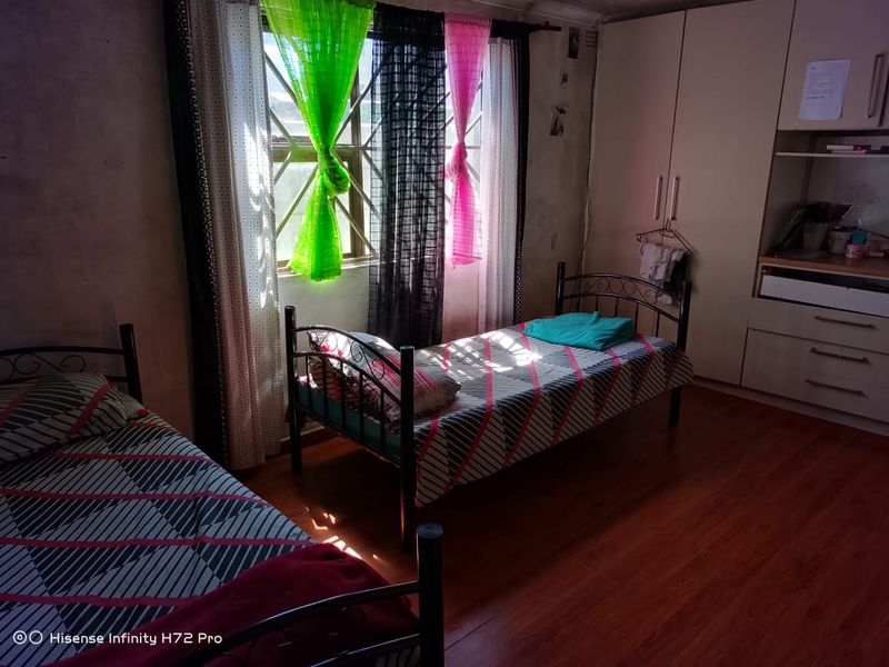 A bedroom featuring laminate flooring, built-in cupboards, and security bars on the window. The walls show signs of wear and require maintenance.