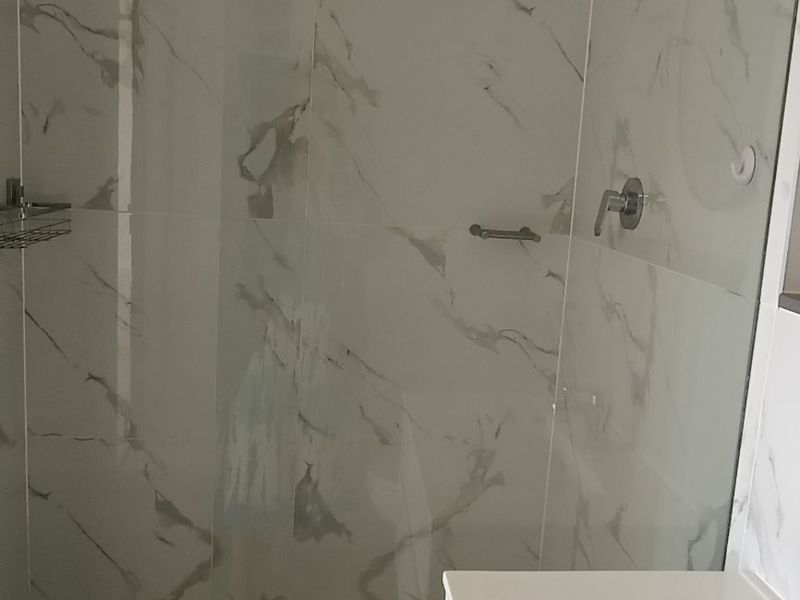 Modern bathroom featuring a walk-in shower with a rainfall shower head, glass screen, and elegant marble-look wall tiling.