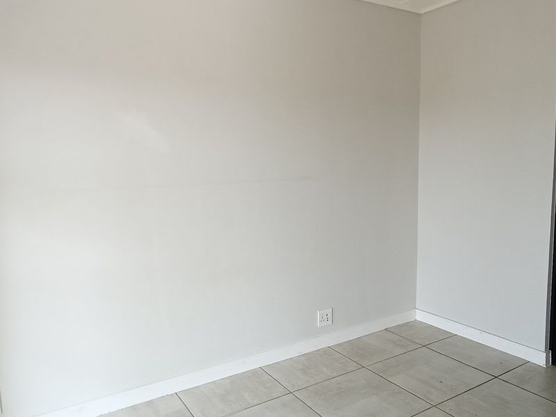 An empty bedroom featuring neutral tiled flooring and a sliding door leading to an en-suite bathroom.