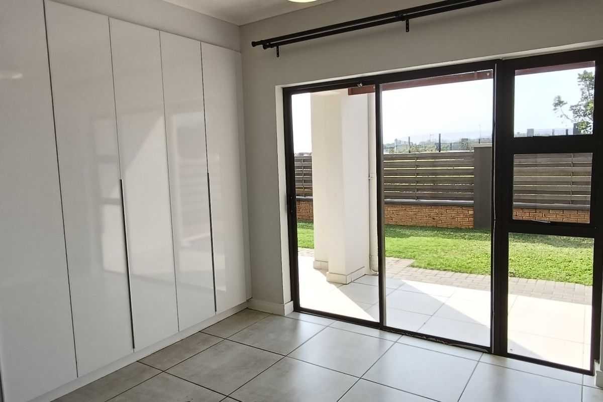 A bright, empty bedroom featuring modern white built-in cupboards, tiled flooring, and a sliding glass door providing direct access to the patio and garden.