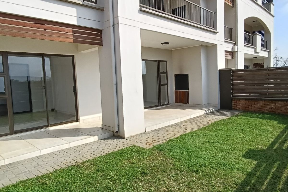 Ground floor apartment featuring a tiled patio with a built-in braai, leading out to a private garden area with a paved walkway.
