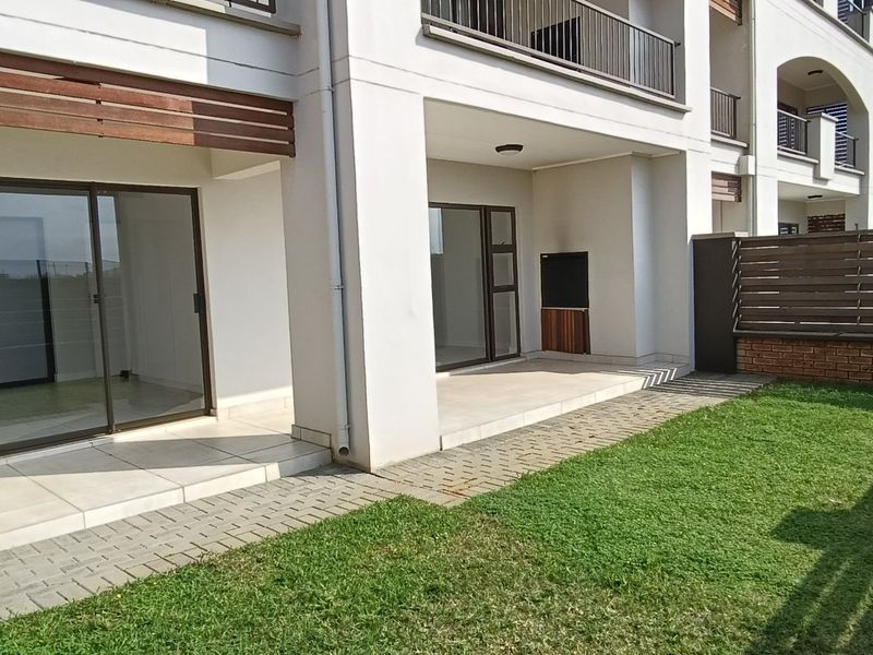 Ground floor apartment featuring a tiled patio with a built-in braai, leading out to a private garden area with a paved walkway.