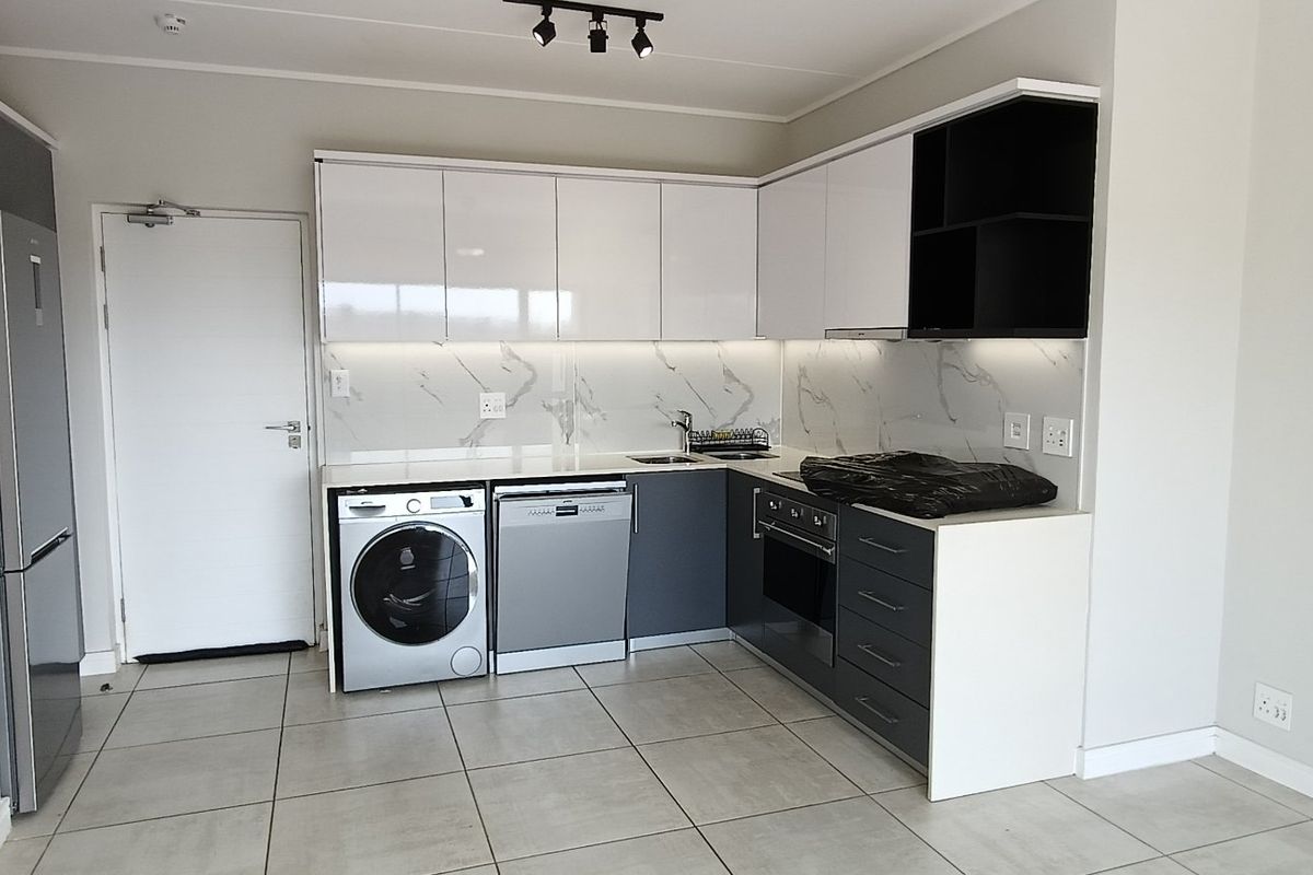 Modern kitchen featuring sleek white and grey cabinetry, marble-look splashback, built-in oven, hob, and tiled flooring in a clean, contemporary apartment setting.