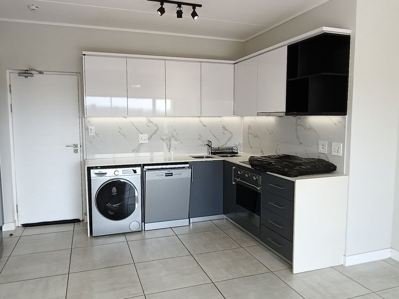 Modern kitchen featuring sleek white and grey cabinetry, marble-look splashback, built-in oven, hob, and tiled flooring in a clean, contemporary apartment setting.