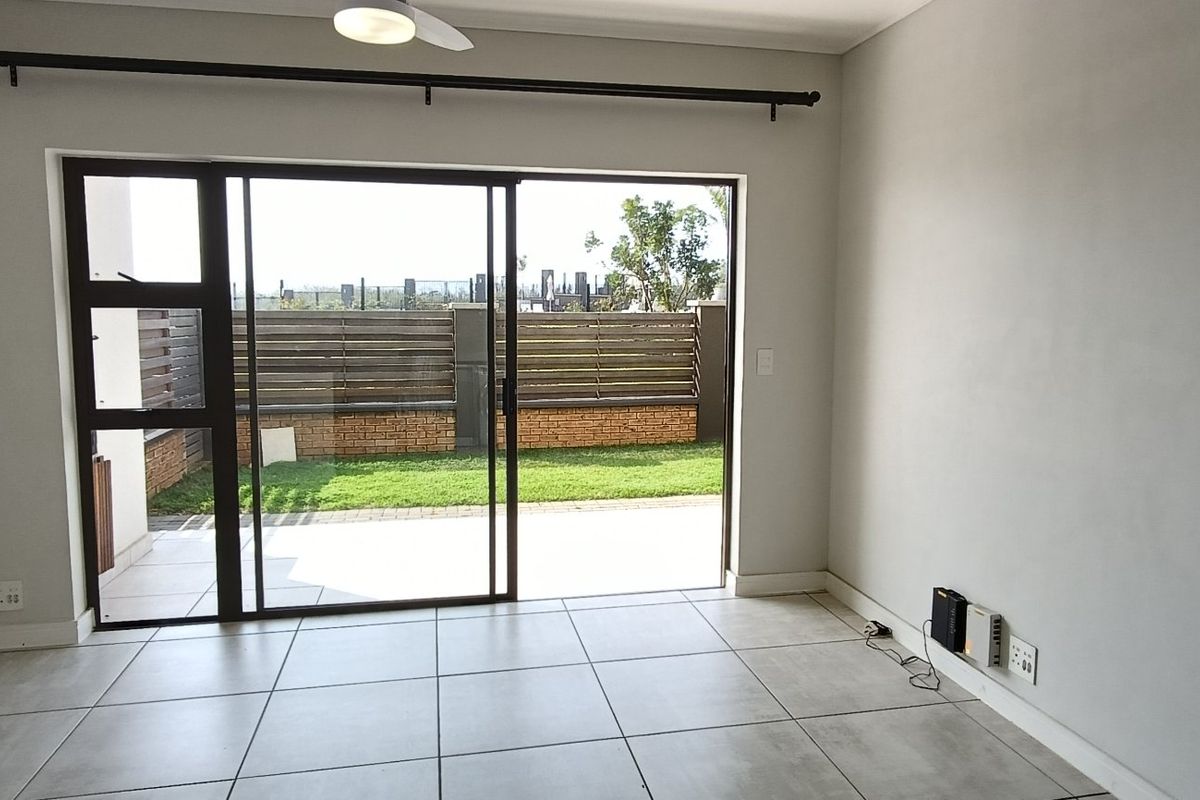 Bright and spacious living area featuring large sliding glass doors that open onto a private patio and garden, finished with neutral floor tiles.